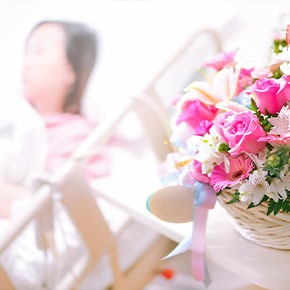Blurred picture of a woman sitting up in a swing bed. There is a basket full of flowers and roses mixed in together.